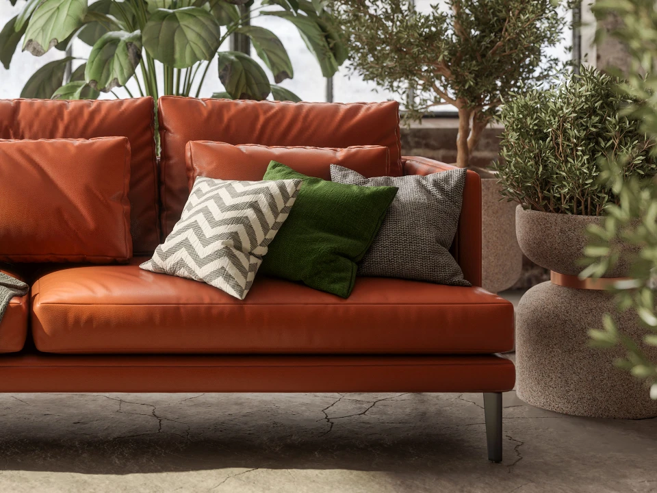 Ein modernes Wohnzimmer mit einem orangefarbenen Ledersofa, das mit drei dekorativen Kissen ausgestattet ist. Hinter dem Sofa stehen große Topfpflanzen.