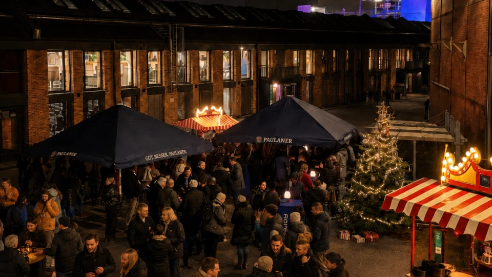 Abendlicher Weihnachtsmarkt mit beleuchteten Ständen und einer Menschenmenge, die sich um Tische unter Sonnenschirmen versammelt, in einem urbanen, industriell wirkenden Umfeld.