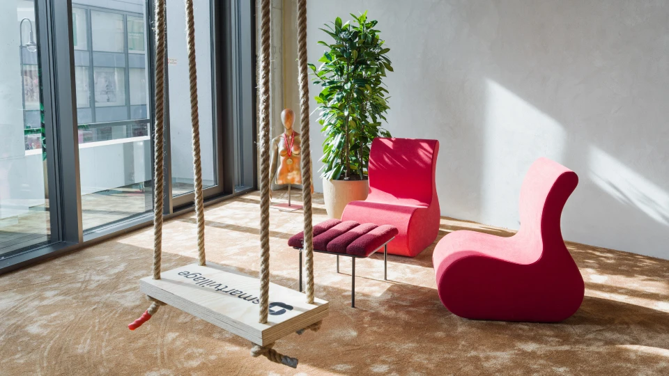 Helles, modernes Büro mit einer Schaukel, rotem Sessel, roter Liege und einer Zimmerpflanze nahe eines großen Fensters.