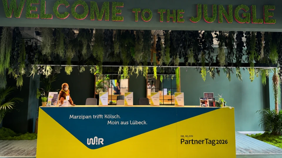 Empfangsbereich mit dem Schriftzug 'WELCOME TO THE JUNGLE' über einem Tresen mit der Aufschrift 'Marzipan trifft Kölsch. Moin aus Lübeck. WJR PartnerTag2026'.
