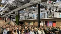 Große Menschenmenge sitzt bei einer Konferenz in einem modernen Saal mit Glasdach und aufwendiger Beleuchtungs- und Tontechnik.