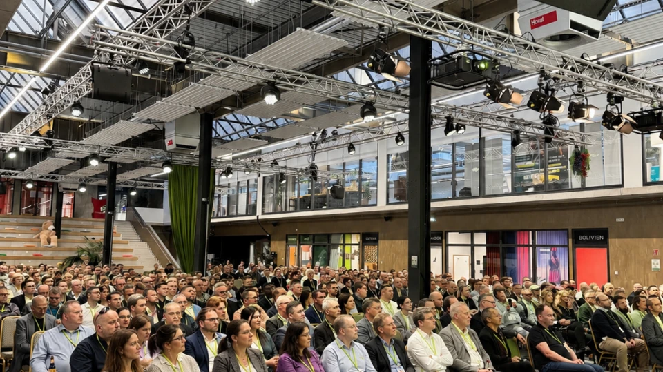 Große Menschenmenge sitzt bei einer Konferenz in einem modernen Saal mit Glasdach und aufwendiger Beleuchtungs- und Tontechnik.