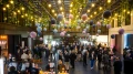 Geschäftige Netzwerkveranstaltung in einer modernen Halle mit hängenden Pflanzen und farbigen Ballons. Menschen stehen in Gruppen, einige unterhalten sich, andere bedienen sich an Buffets.