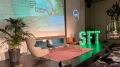 Eine Konferenzbühne mit SFT-Leuchtschild, vier Sesseln, darunter ein Teppich, zwei Pflanzen und eine Präsentationsleinwand mit der Aufschrift 'Founders League'.